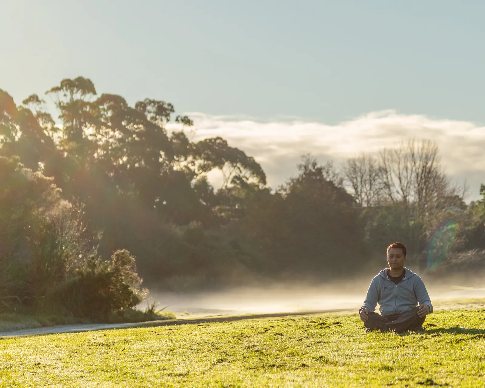 Zhi Lee meditating in Waitarua Reserve, with a forested valley and distant hills in the background
